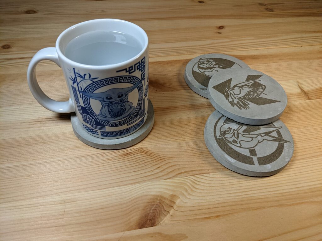 4 cement coasters laser engraved with birds, shown with a Grogu mug